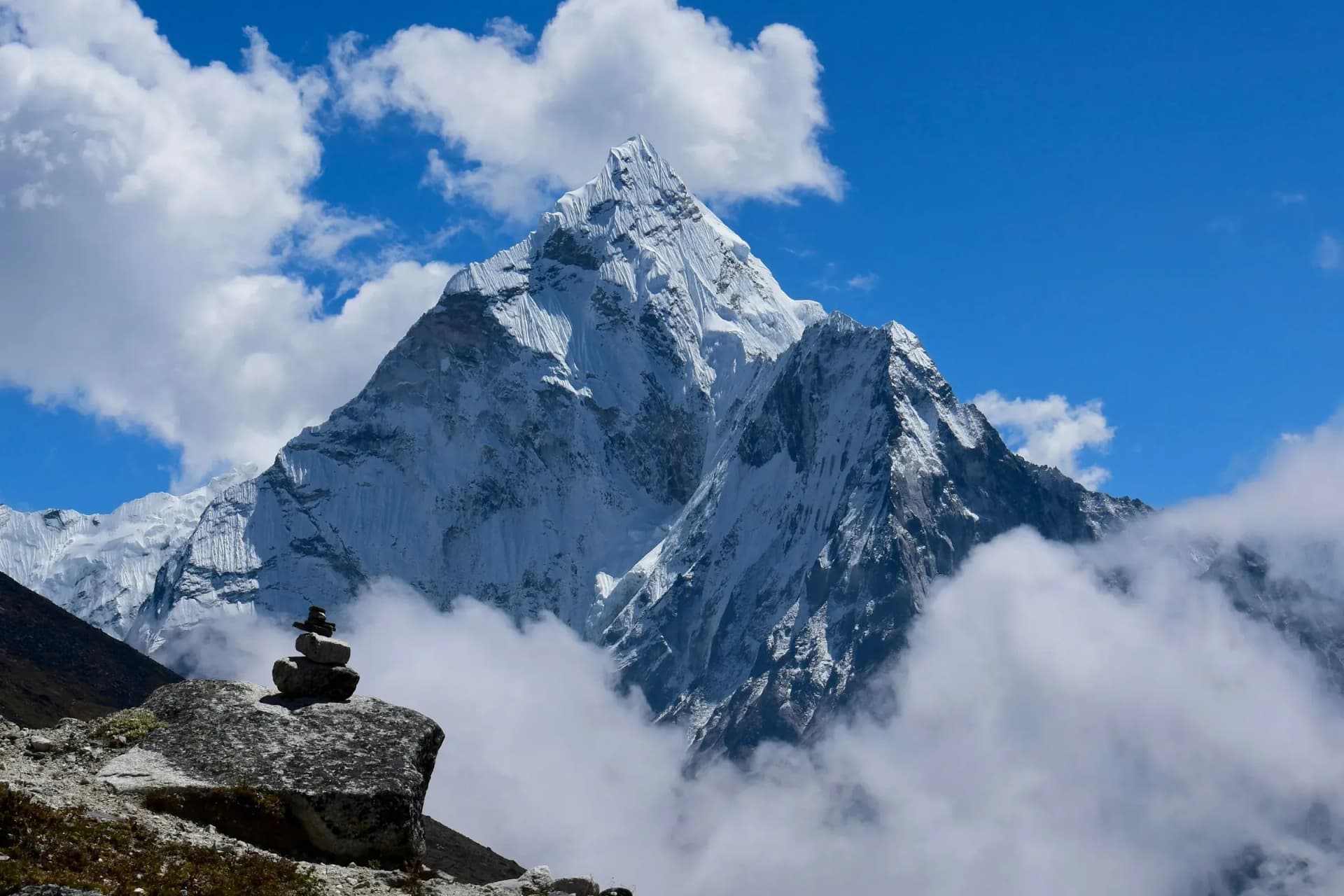 Ama Dablam rising above the clouds with a stone cairn in the foreground