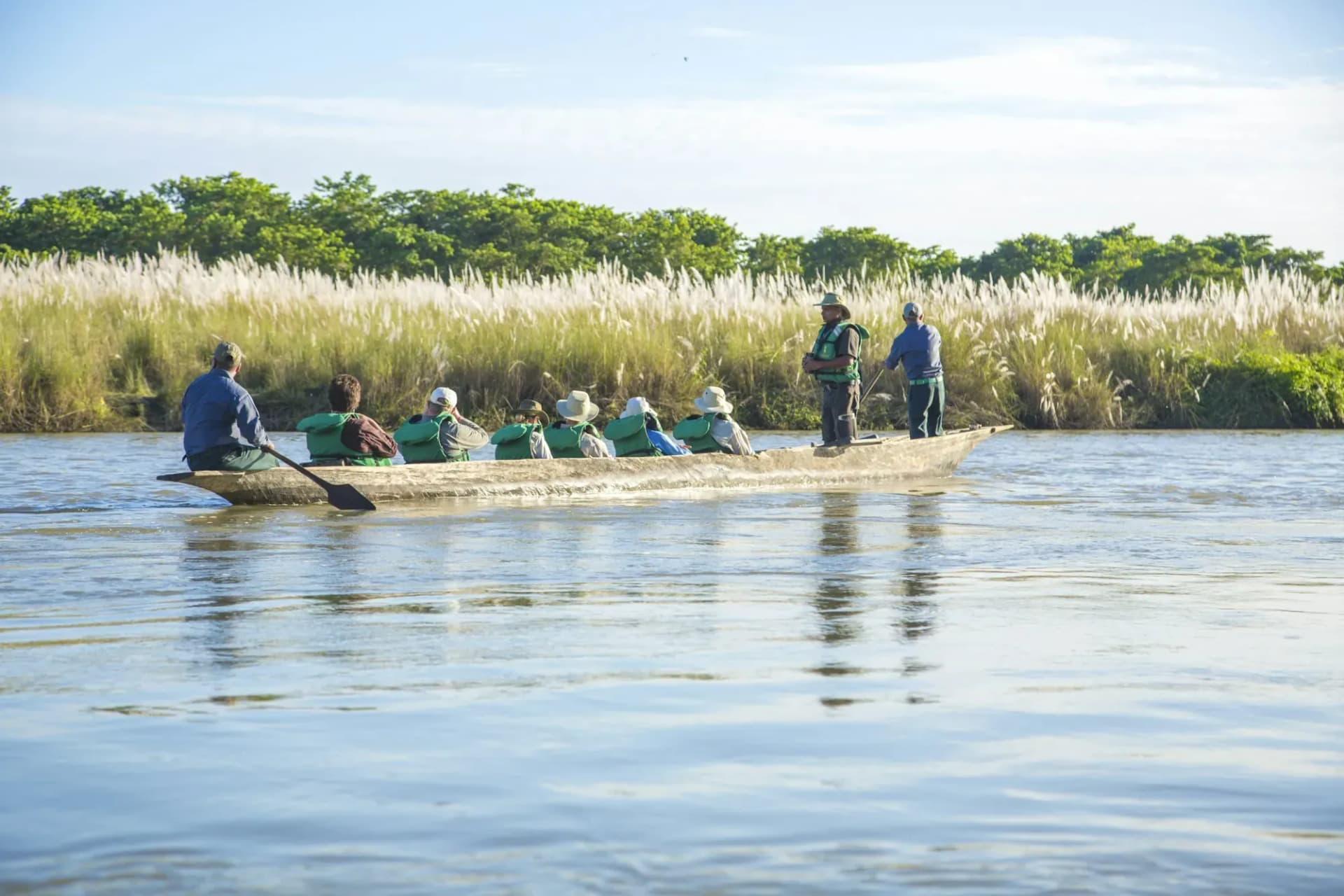 Guests in a dugout canoe on a river lined with tall grass