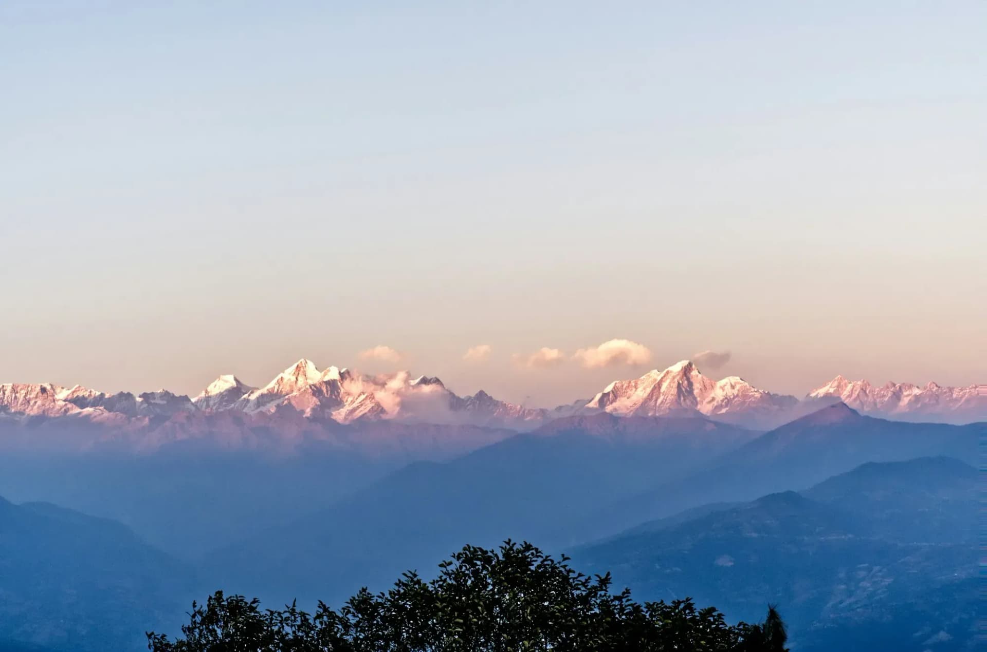Pink dawn light on a long Himalayan range above blue hills