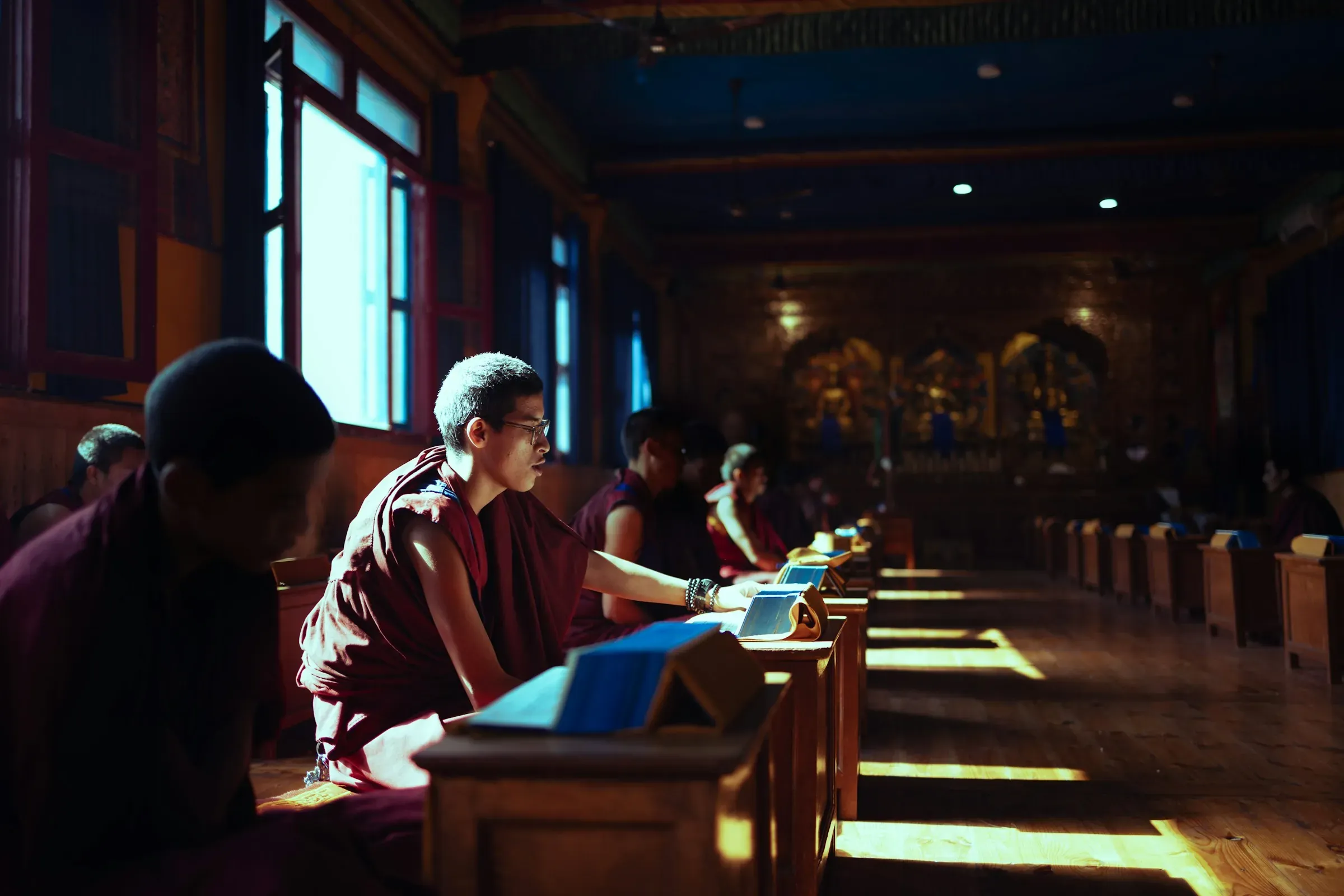 Buddhist monks studying scriptures in a sunlit monastery hall