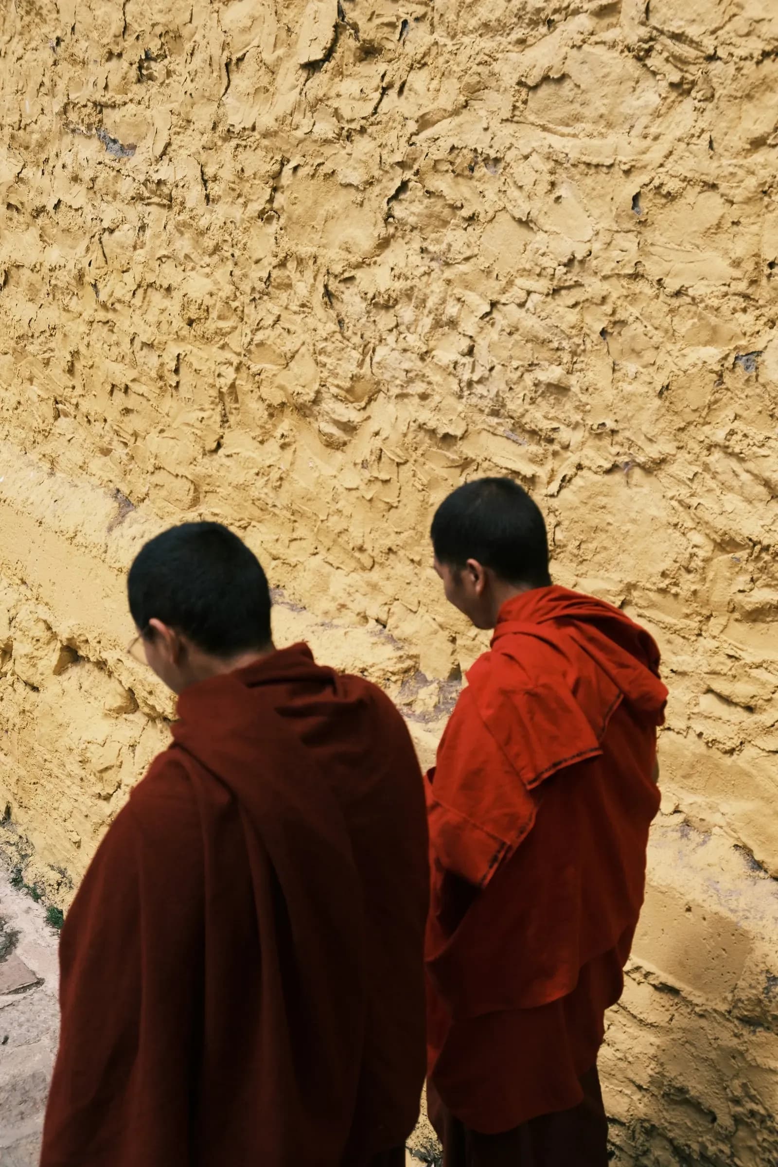 Two monks in maroon robes beside a monastery wall