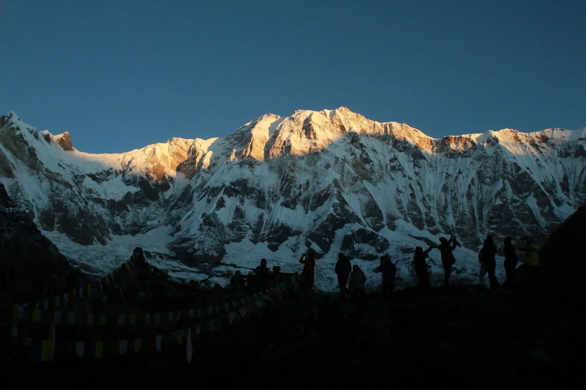 Sunrise lighting a great Himalayan wall, with walkers silhouetted below