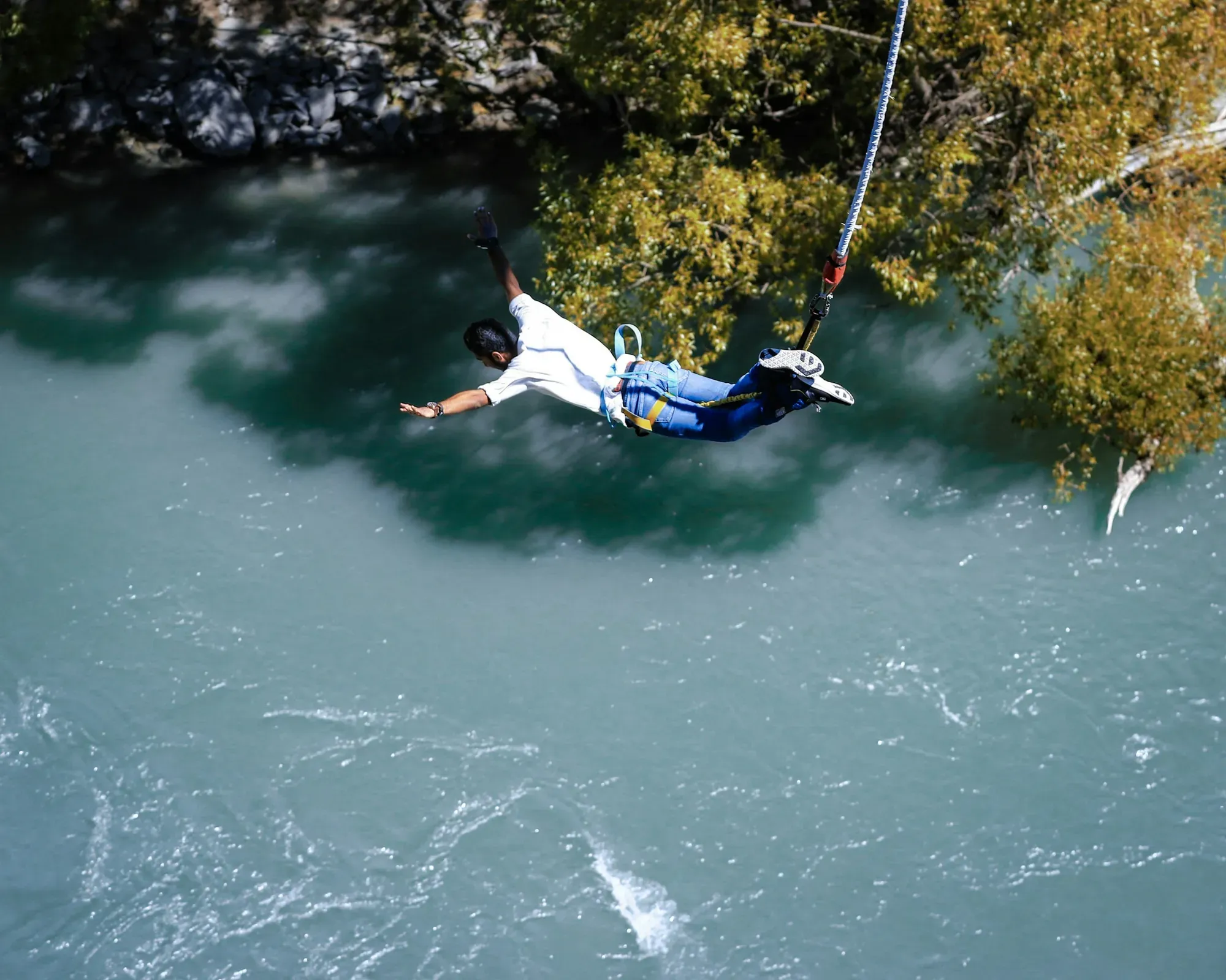 A bungee jumper diving head-first above a turquoise river