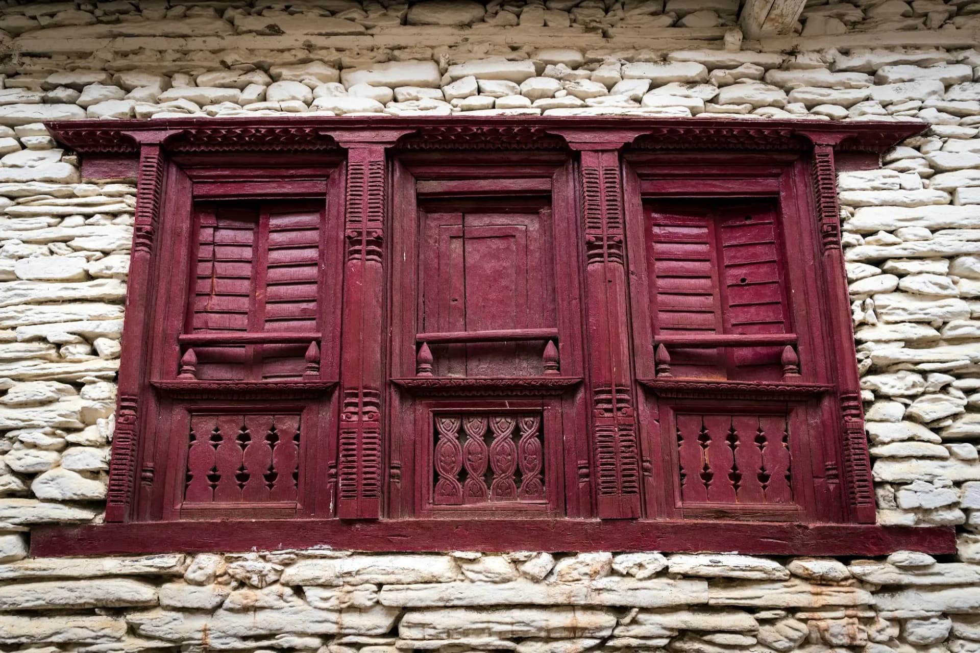 Carved maroon wooden window in a whitewashed stone wall
