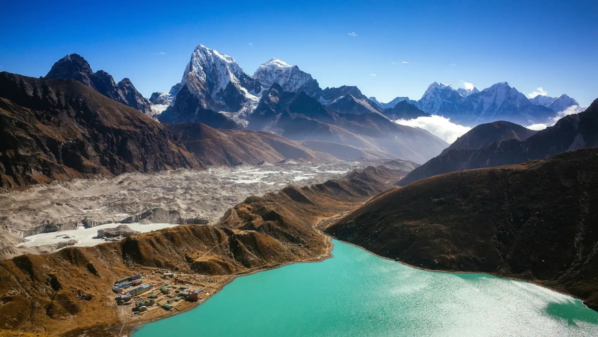 Turquoise Gokyo lake and its lodges beside the Ngozumpa Glacier, with Cholatse and Taboche behind