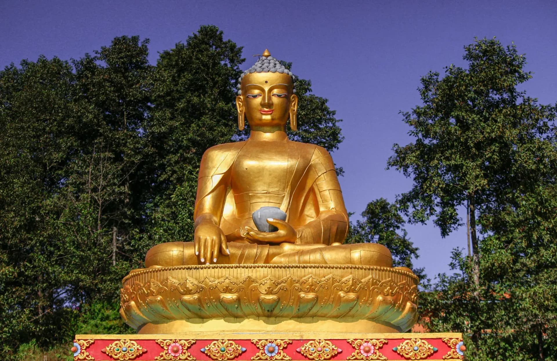 Golden seated Buddha statue among green trees