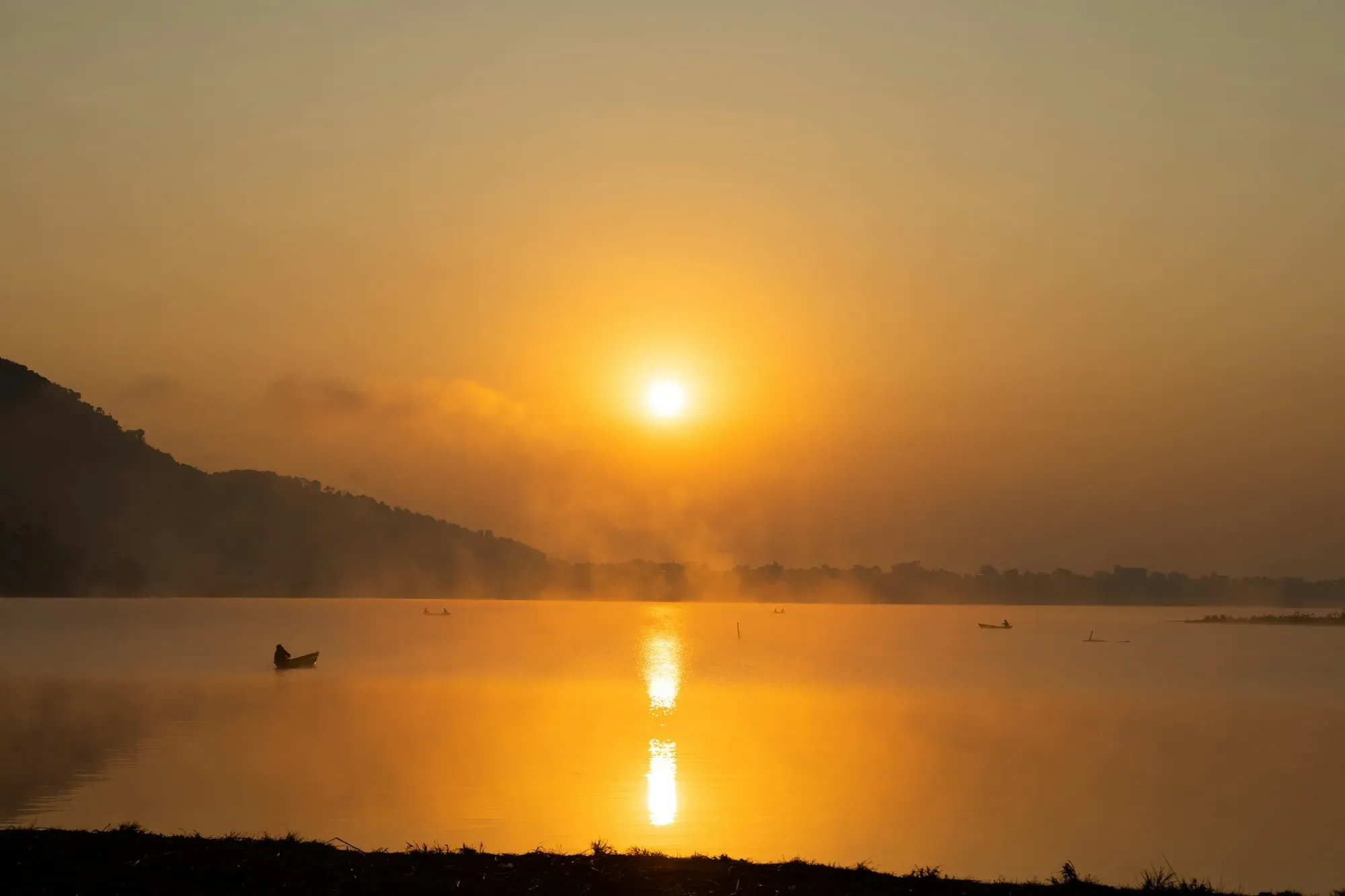 Golden sunrise over a calm lake with a lone boat