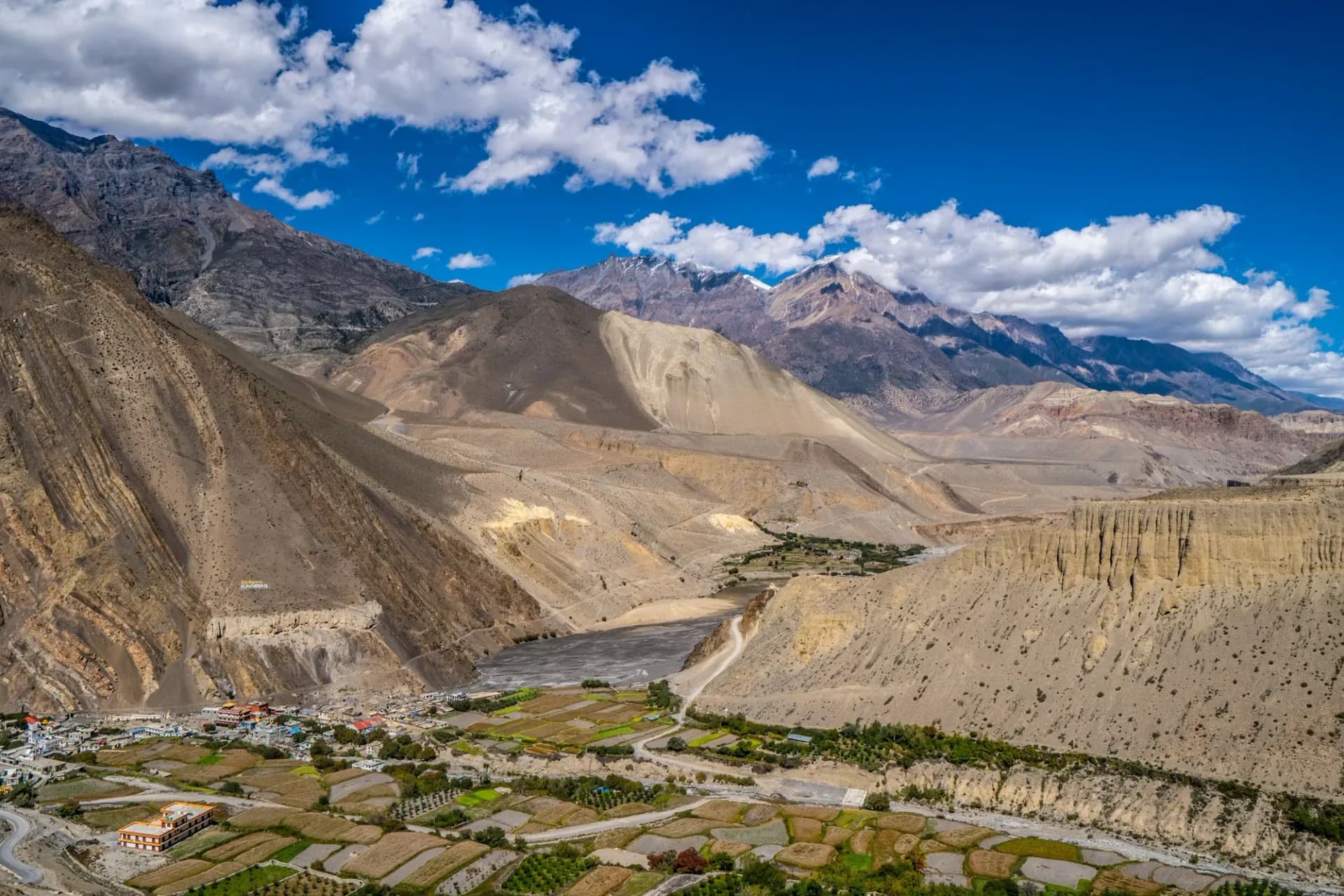 Green fields and a village below eroded cliffs in an arid Himalayan river valley