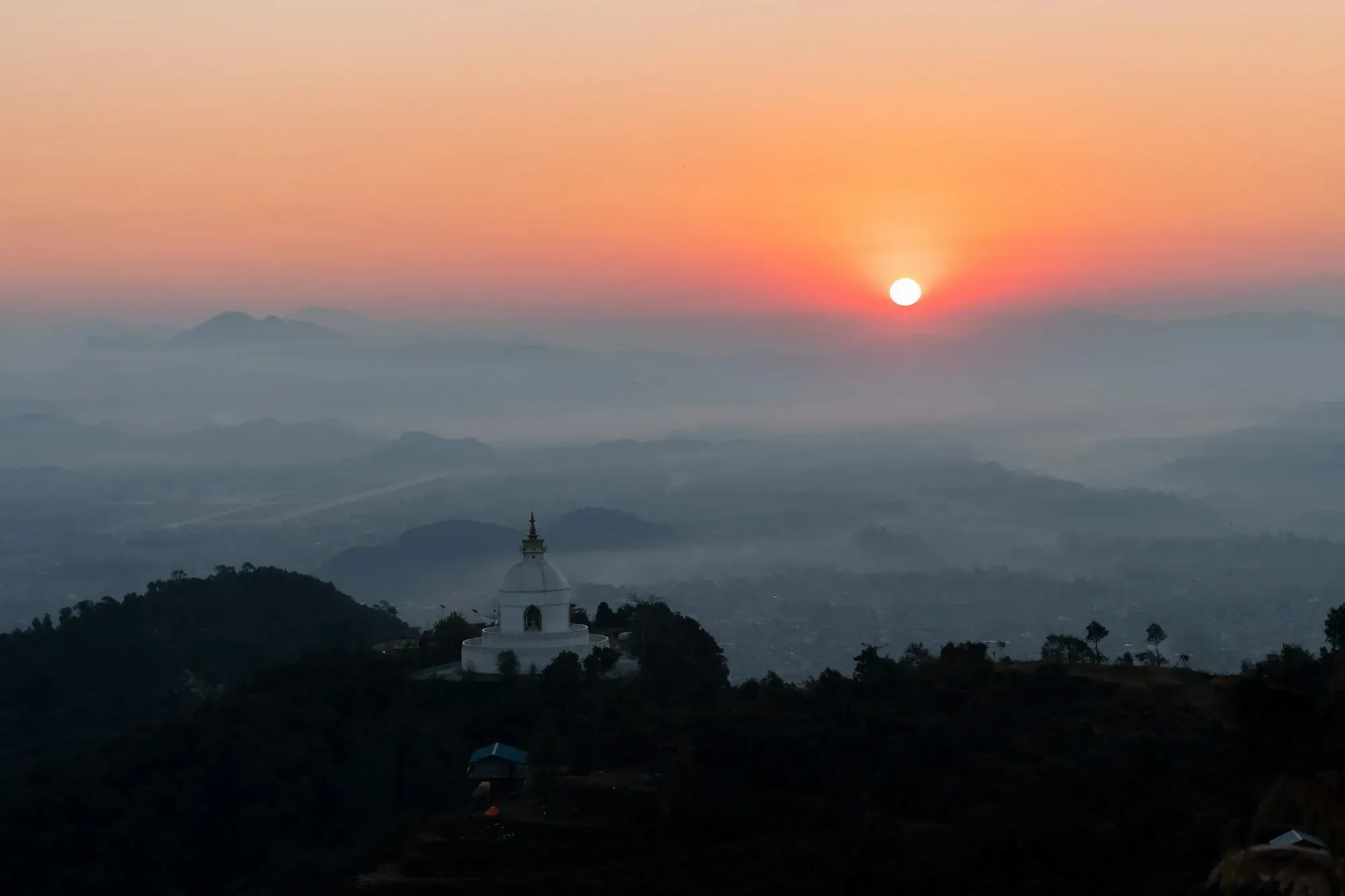 White peace pagoda on a forested ridge above a misty valley at sunrise