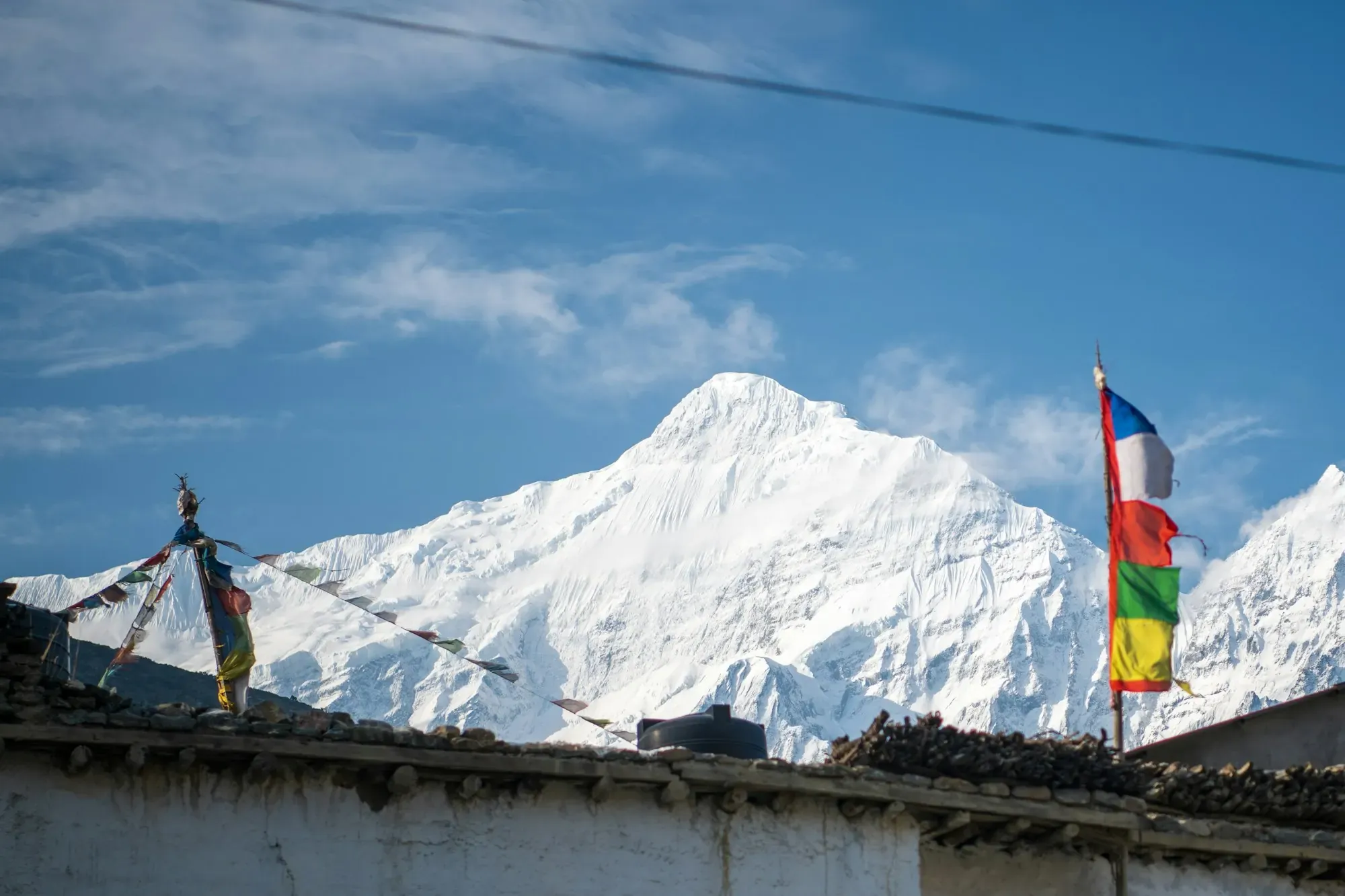 Snow peak above a rooftop stacked with firewood and prayer flags